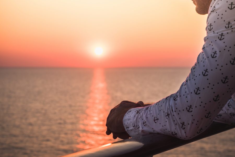 Men's hands on the railing of a cruise ship against the backdrop of sea waves and a fantastic sunset. Sea cruises and rest